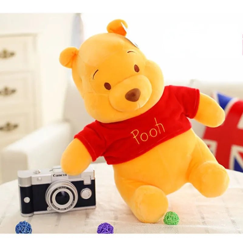 Plush toy bear wearing a red shirt with 'Pooh' on it, next to a camera and small flags.