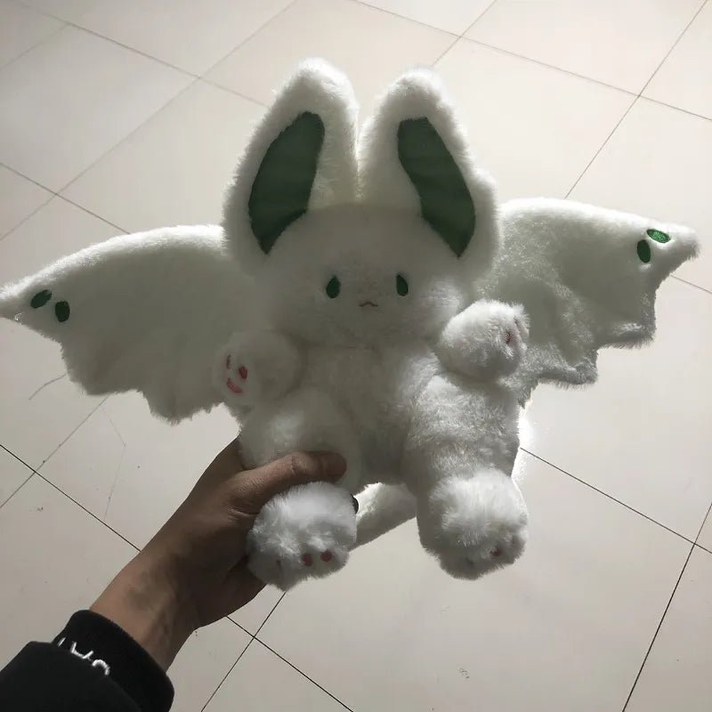 White plush toy with bat wings held by a hand on a tiled floor