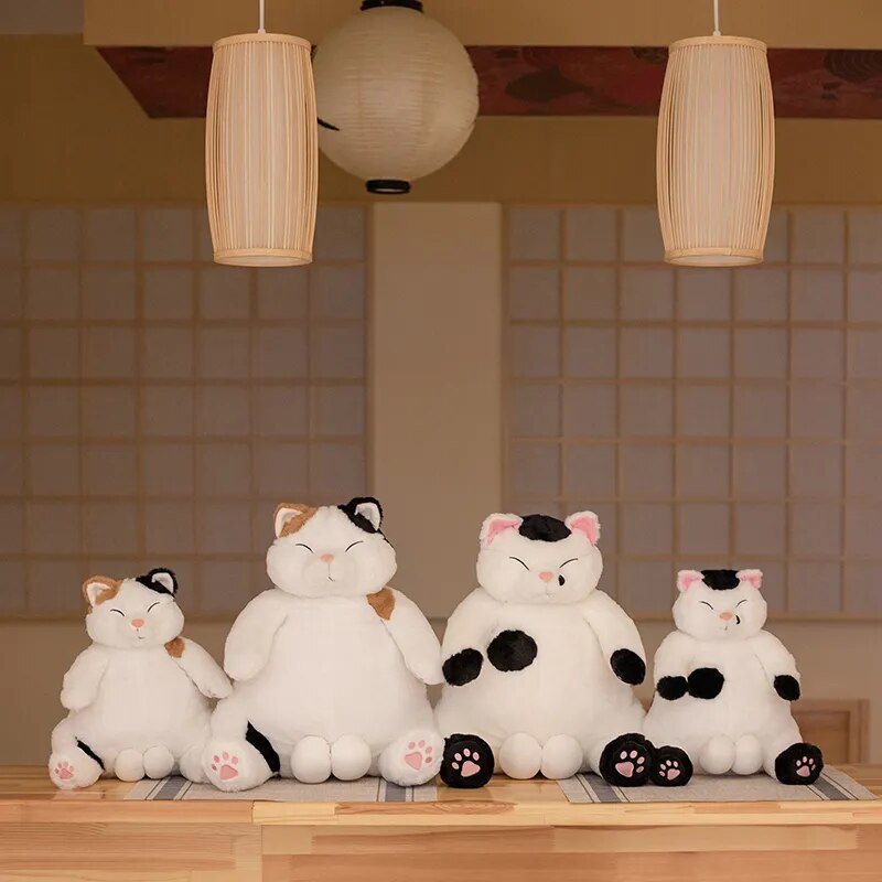 Four plush cat toys on a wooden surface with a tiled wall and hanging lights in the background.