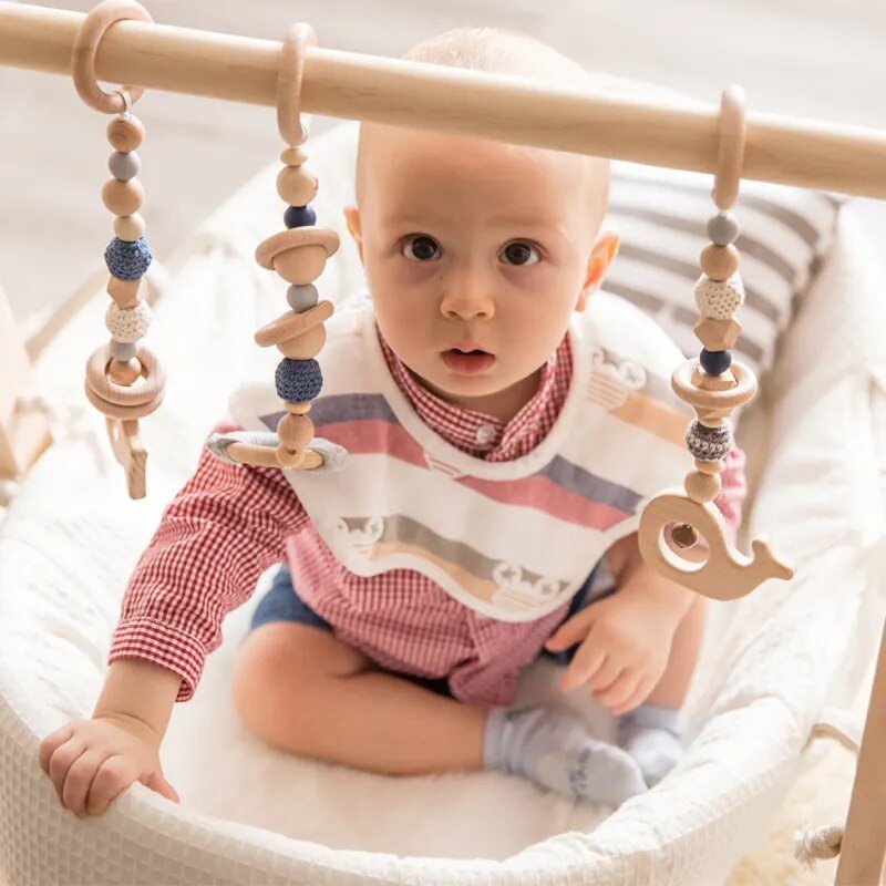 Baby sitting in a crib with a wooden crib bar and hanging toys.