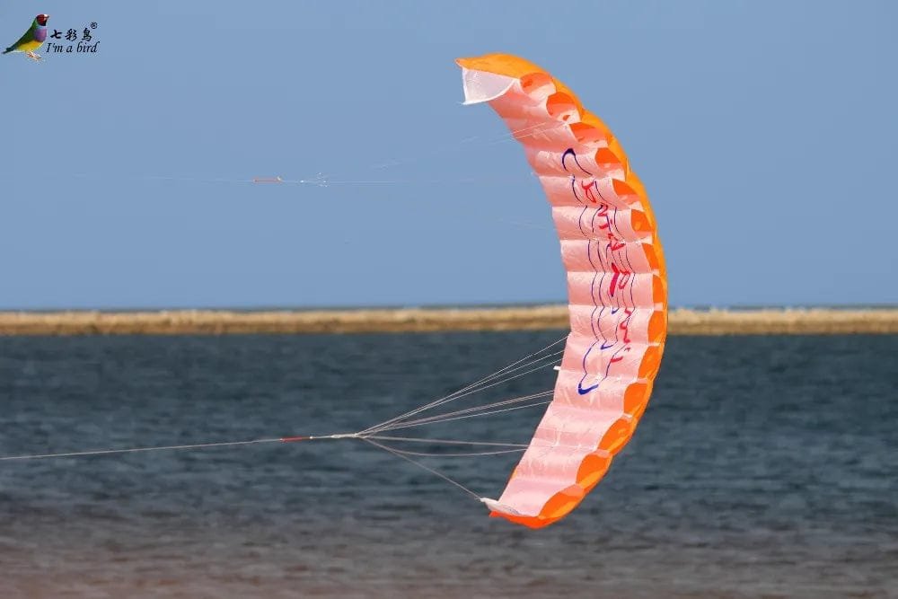 Orange and pink parafoil kite flying over a body of water with a clear blue sky.