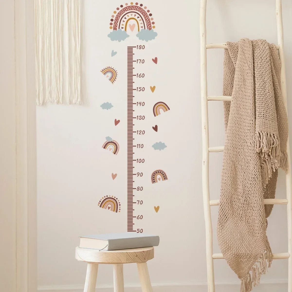 Wall growth chart with rainbow and heart design on a light wall next to a ladder and stool.
