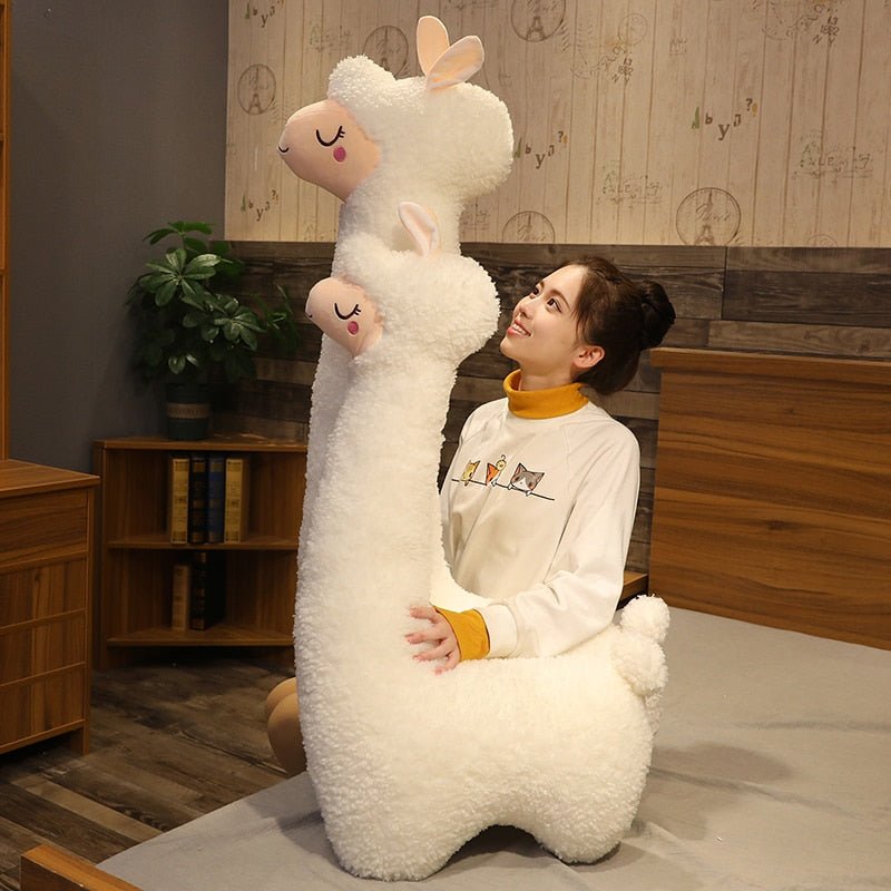 Person sitting on a large plush llama toy in a room with wooden furniture and a plant.