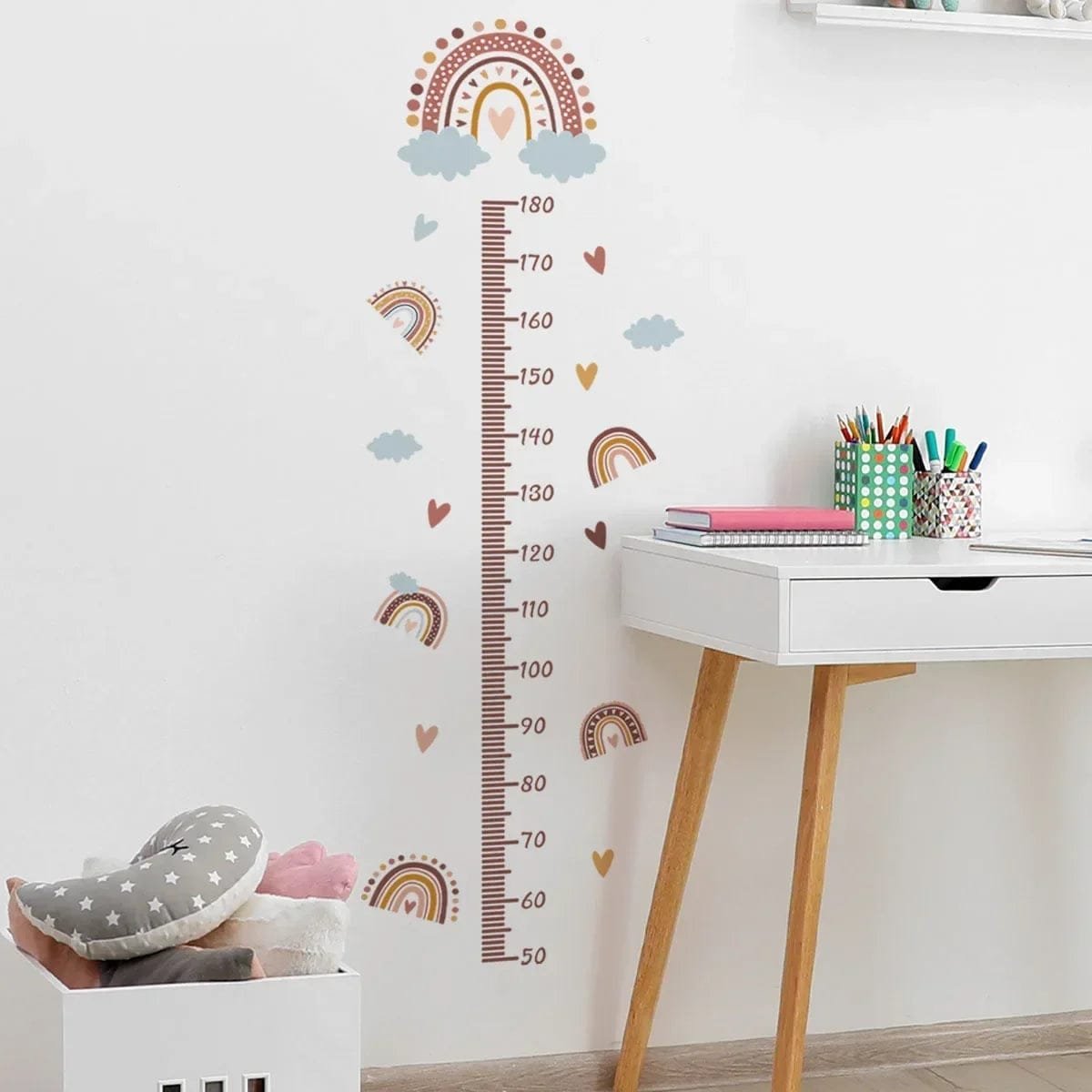 Growth chart with rainbow and cloud design on a wall next to a white desk.