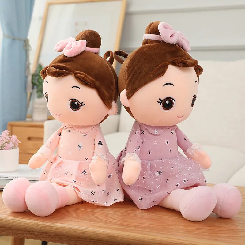 Two plush toys with brown hair and pink bows sitting on a wooden surface.