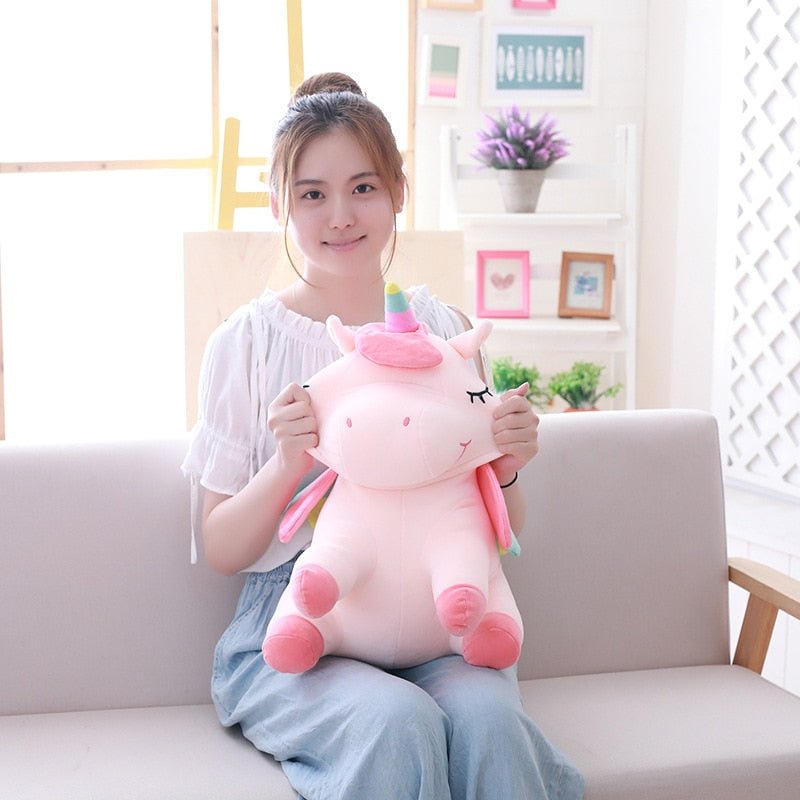 Woman holding a large pink unicorn plush toy in a living room setting.