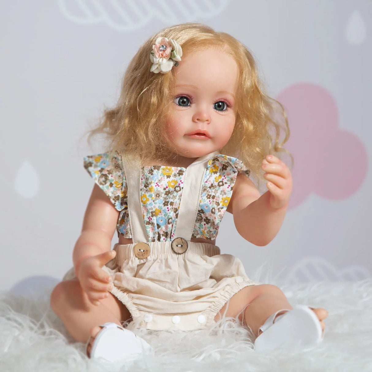Doll with blonde hair and floral outfit sitting on a white surface with a soft pink heart in the background.
