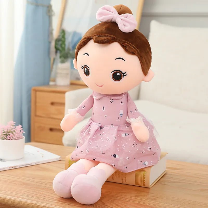Plush toy doll with brown hair and a pink dress sitting on a wooden surface.