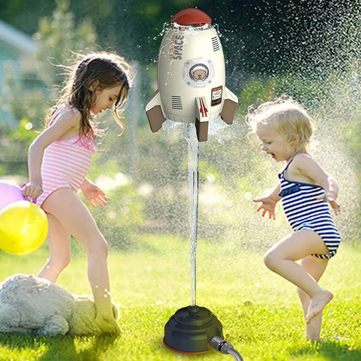 Children playing with a rocket-shaped sprinkler in a grassy area.