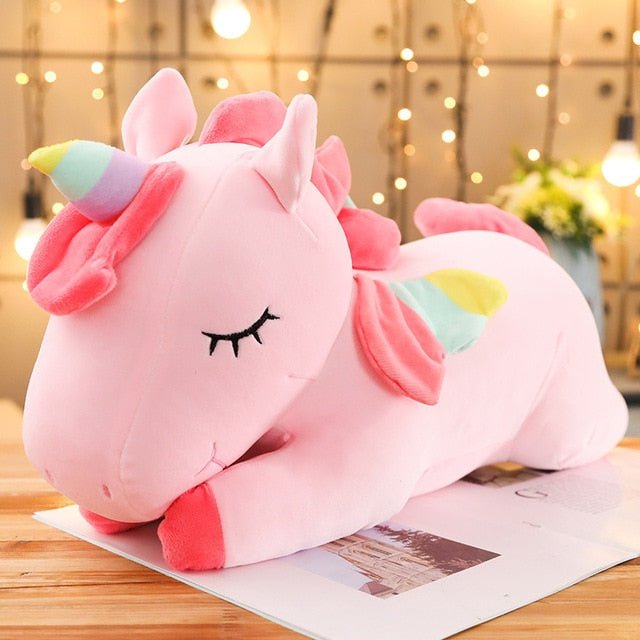 Pink unicorn plush toy on a wooden surface with a blurred background