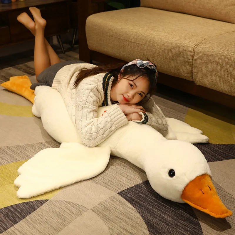 Person lying on a large plush swan toy on a checkered floor.