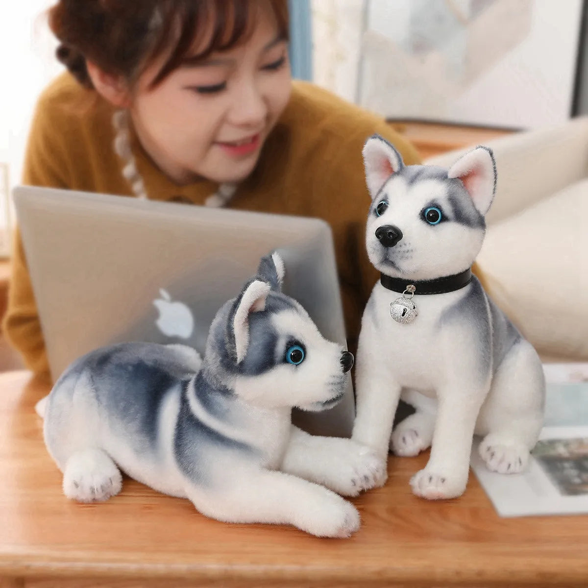 Two husky plush toys on a table with a person using a laptop in the background.