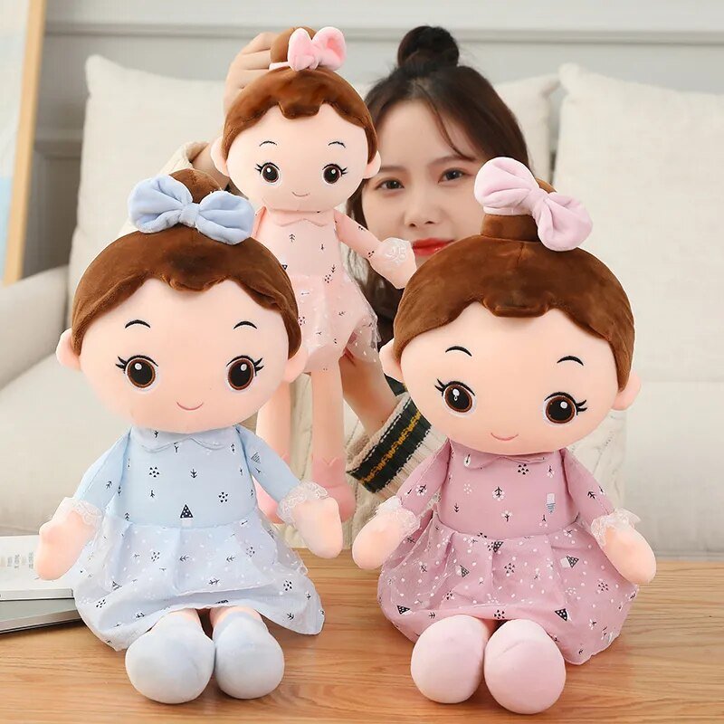 Three plush toys with different outfits on a wooden surface, with a person partially visible.