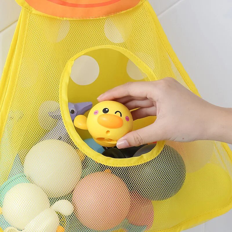 Yellow mesh storage bag with bath toys, including a yellow rubber duck, on a tiled bathroom floor.