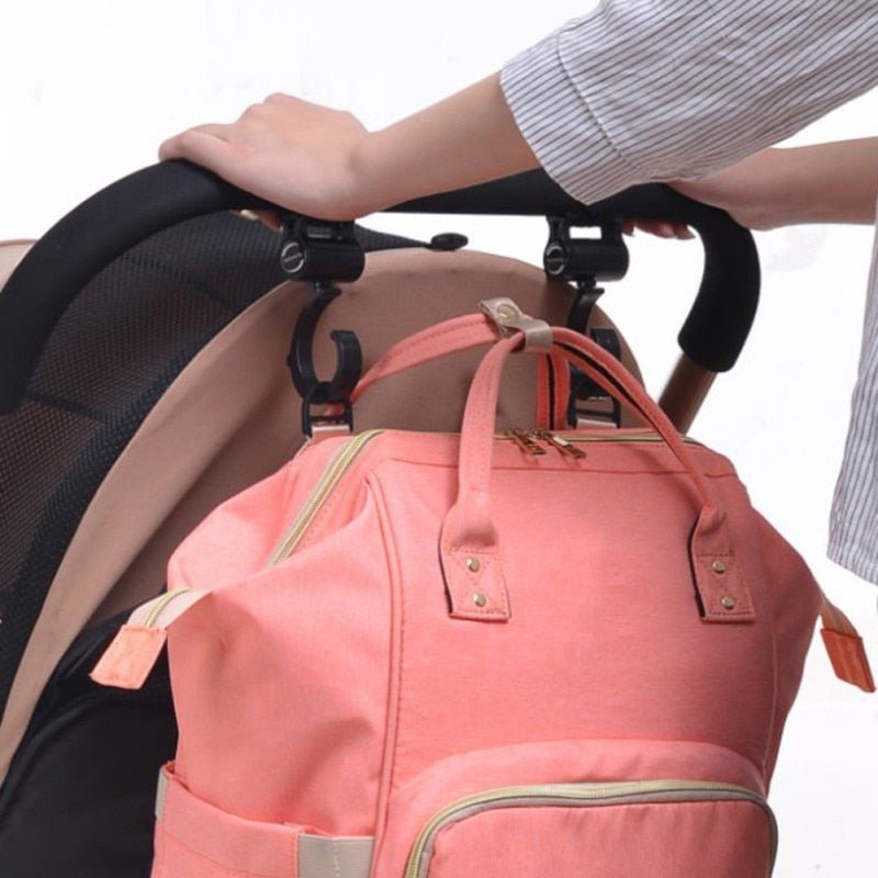 Pink backpack attached to a stroller with a hand holding onto the stroller.