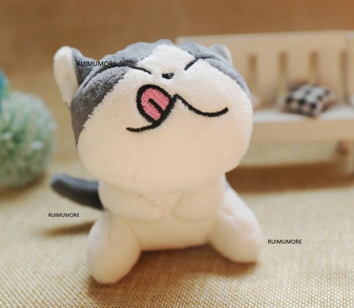 Plush toy resembling a cat with a gray hat on a beige surface.