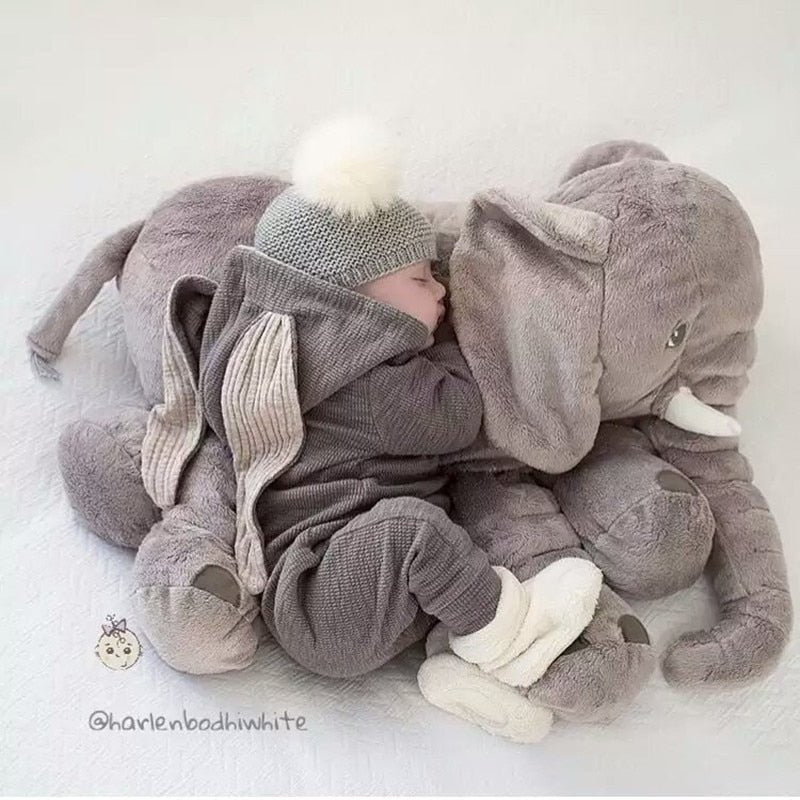 Child in a gray outfit lying next to a large plush elephant toy.