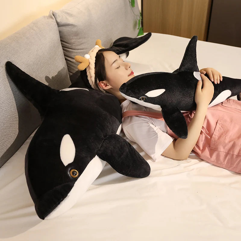 Person lying on a bed with a large black and white plush toy shaped like a whale.