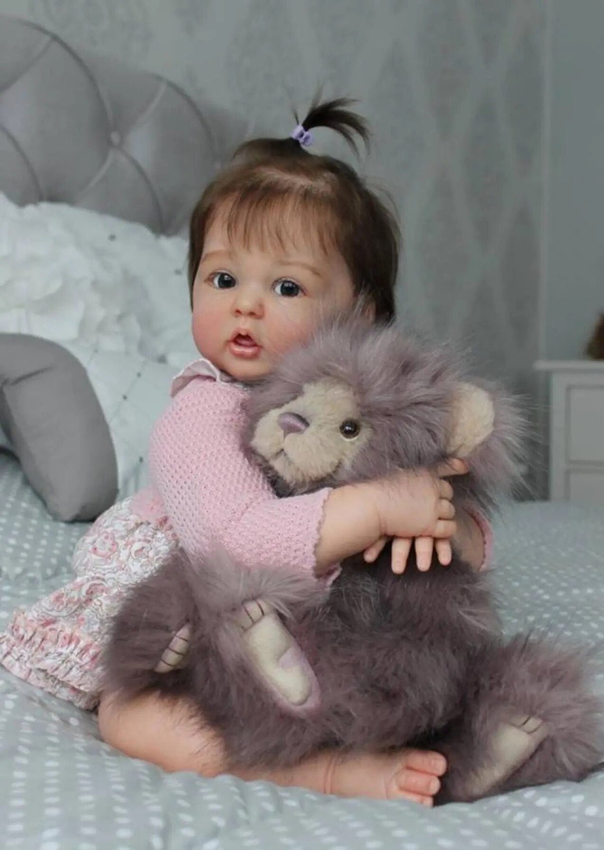 Reborn doll holding a plush lion toy on a bed