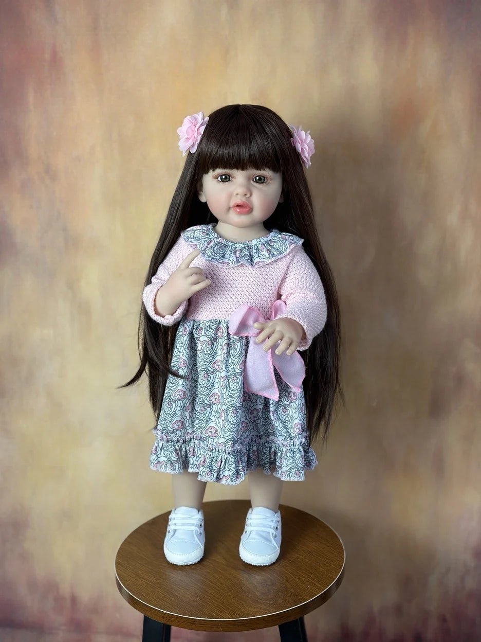 Doll with long dark hair and a floral dress on a wooden stool.