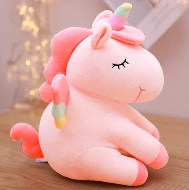 Pink unicorn plush toy on a wooden surface.