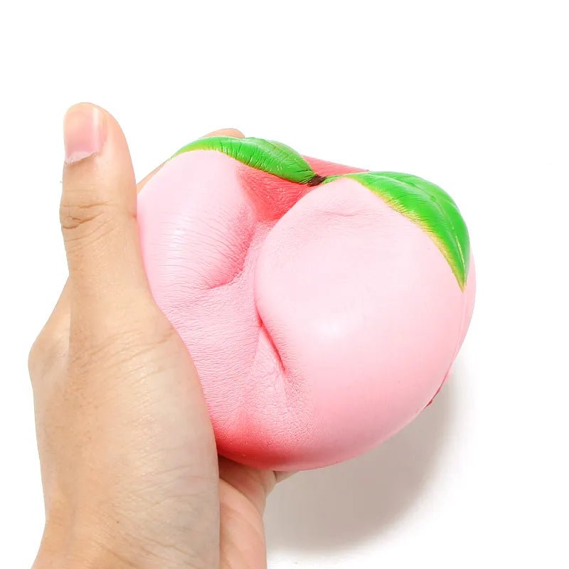 Pink squishy peach toy held in a hand against a white background