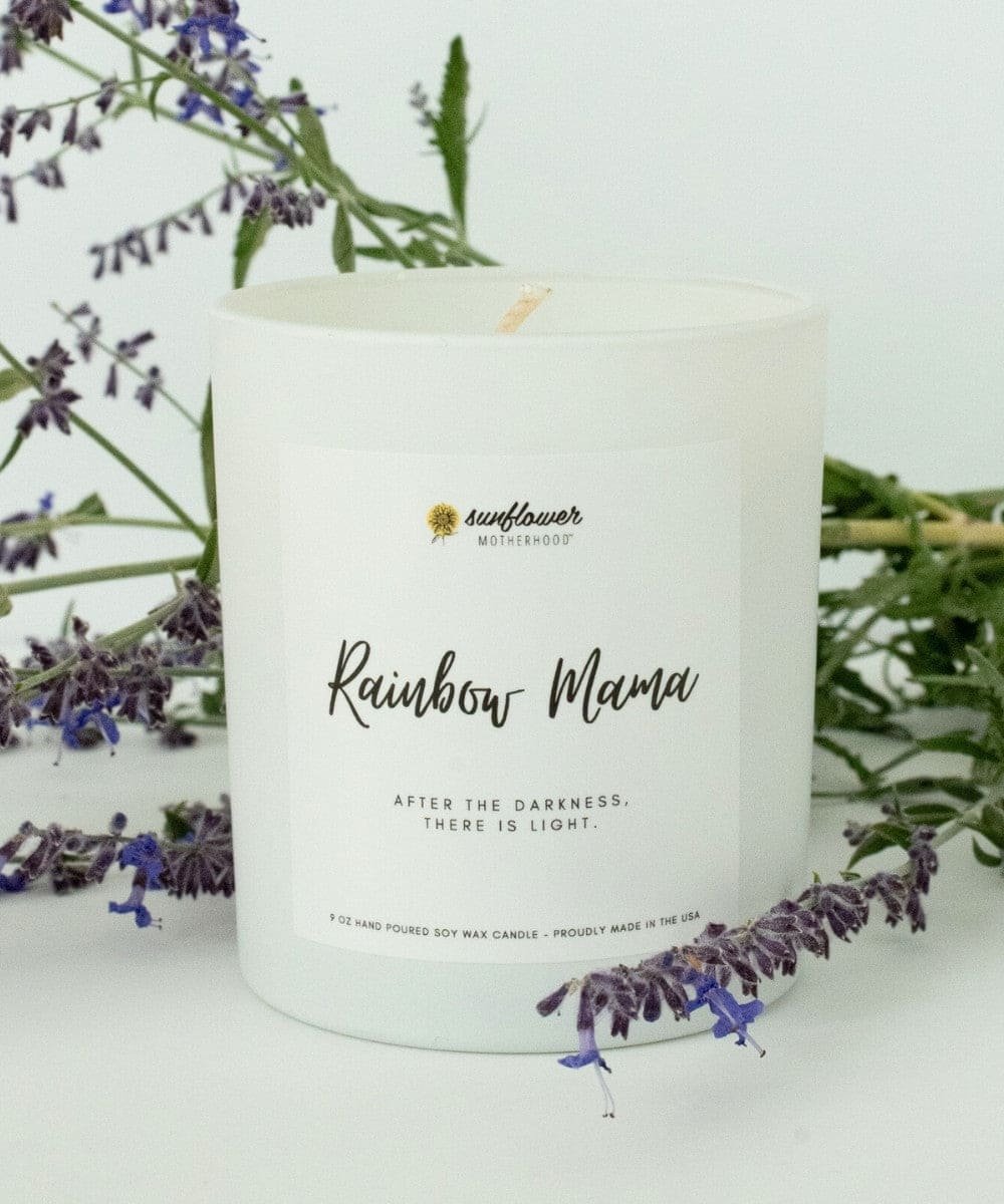Candle with 'Rainbow Mama' text and sunflower branding, surrounded by lavender flowers.