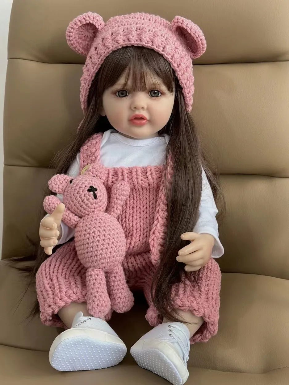 Doll wearing a pink outfit with a teddy bear and matching hat on a brown background
