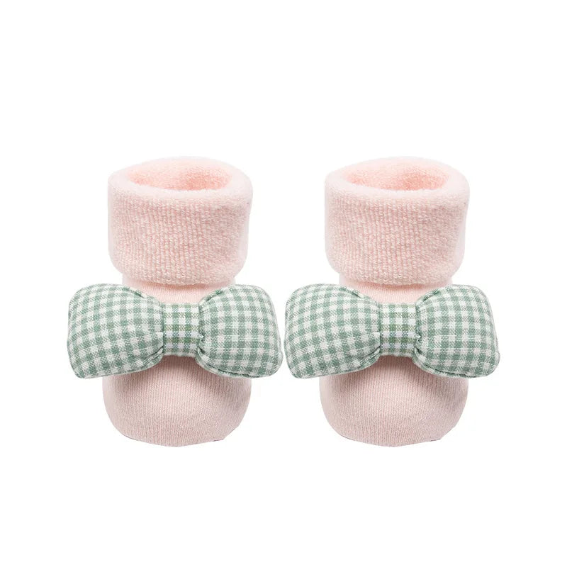 Pair of baby booties with pink fuzzy tops and green checkered bows on a white background