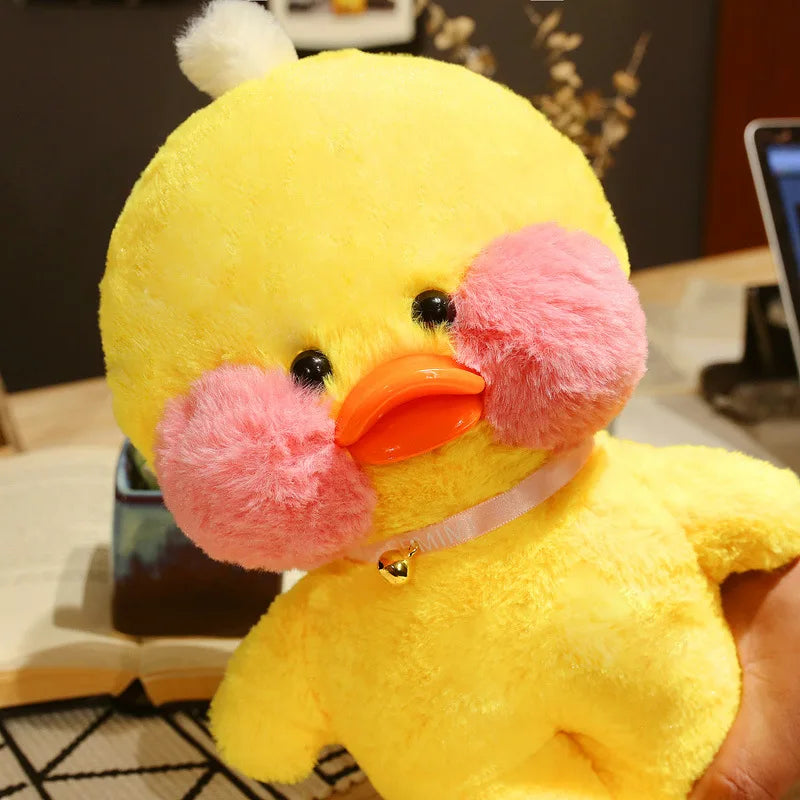 Yellow plush duck with pink cheeks and an orange beak on a blurred indoor background