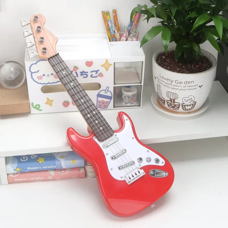 Red toy guitar on a white surface with a plant and stationery items in the background