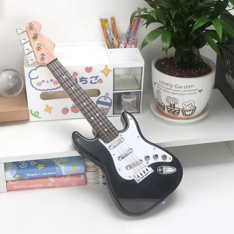 Black electric guitar on a white surface with stationery items and a plant in the background