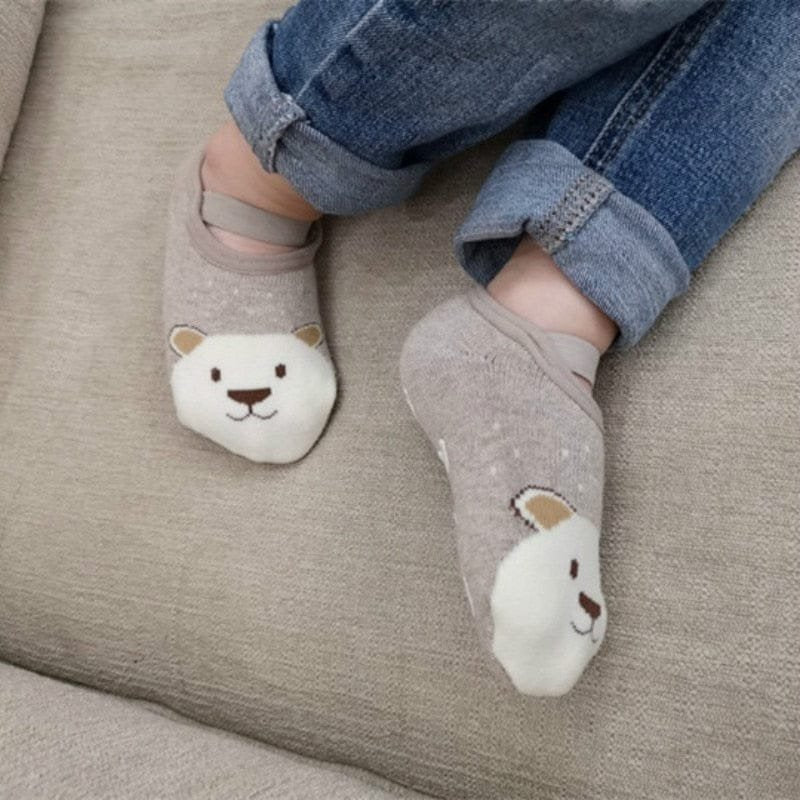 Gray socks with bear faces worn by a person on a beige couch.