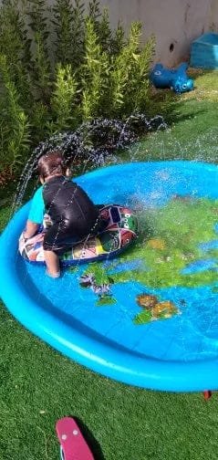 Child playing in a small blue inflatable pool with water splashing around