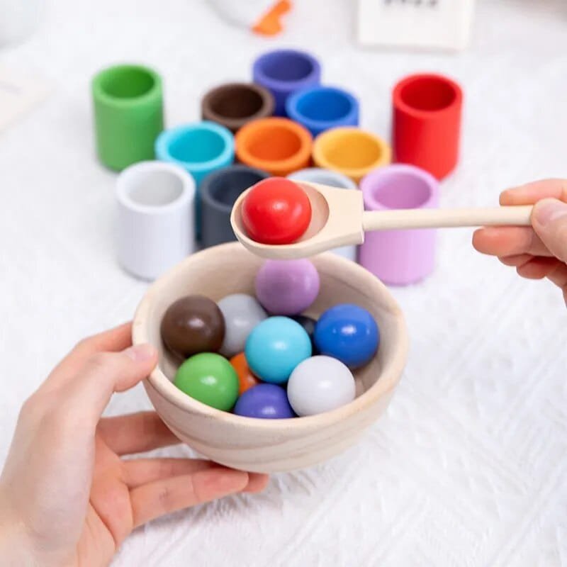 Colorful balls in a wooden bowl with a wooden spoon, surrounded by color blocks.