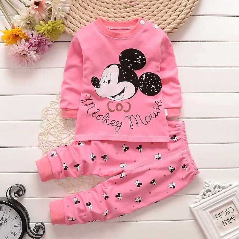 Pink children's outfit with Mickey Mouse design on a wooden surface with flowers and a clock.