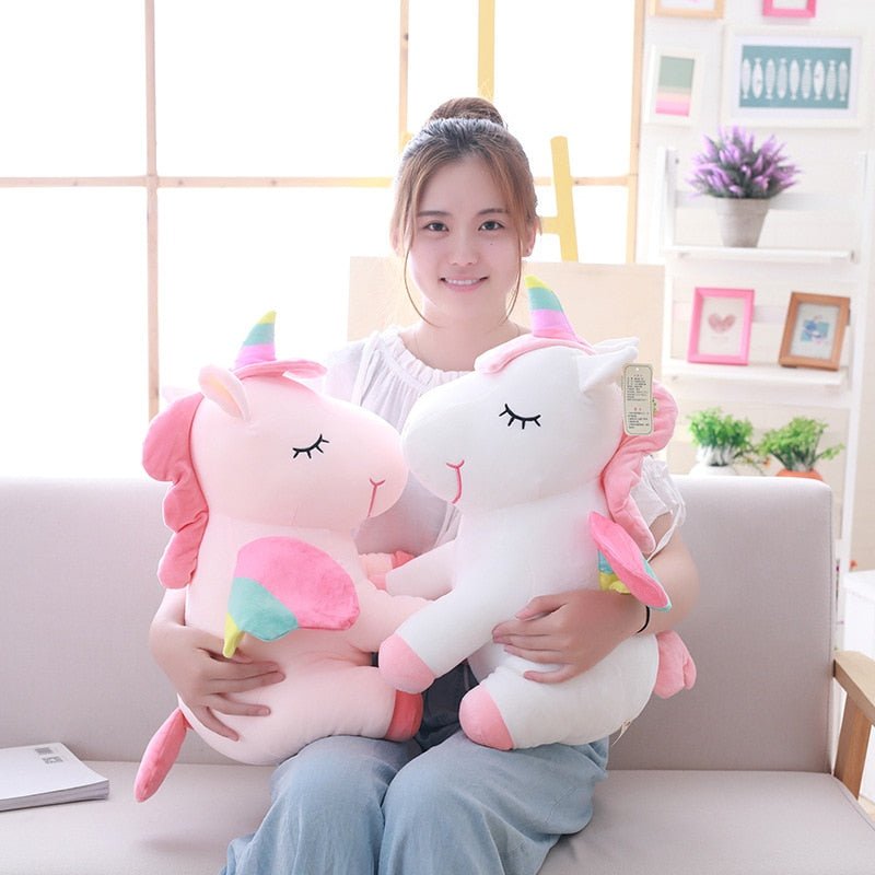 Woman holding two large plush unicorn toys in a living room setting.