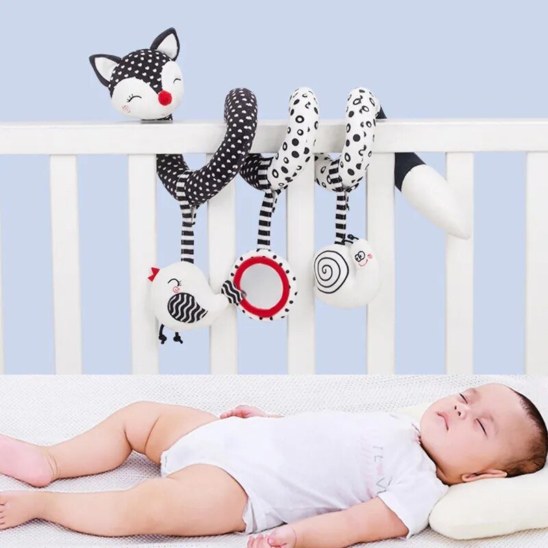 Baby lying in a crib with colorful baby toys hanging over the side.