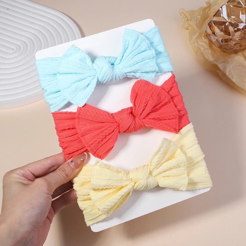 Three colorful bow-shaped hair accessories on a white plate with a hand holding one of them.