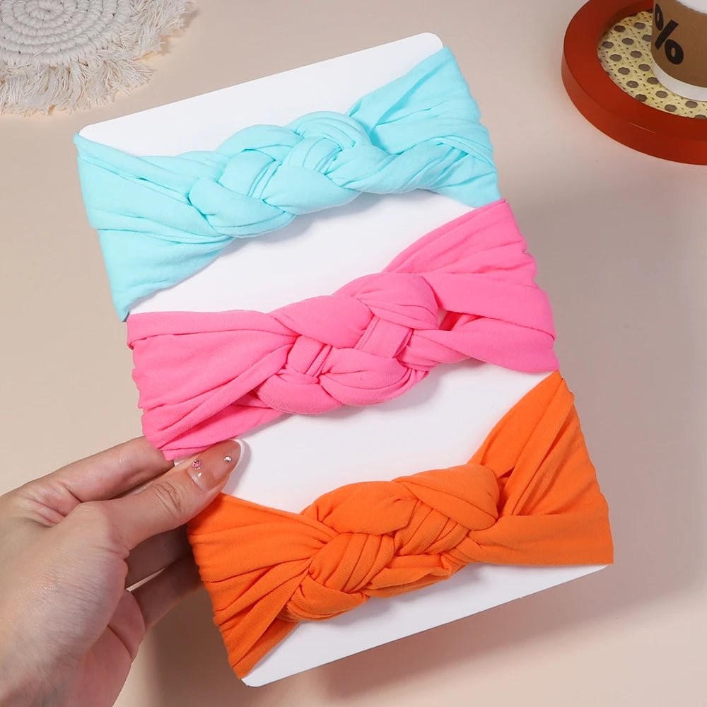 Three colorful knotted headbands in blue, pink, and orange on a white surface.