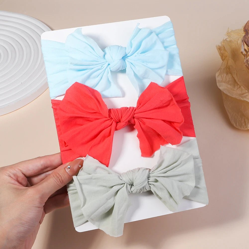 Three colorful hair bows on a white card held by a hand against a beige background