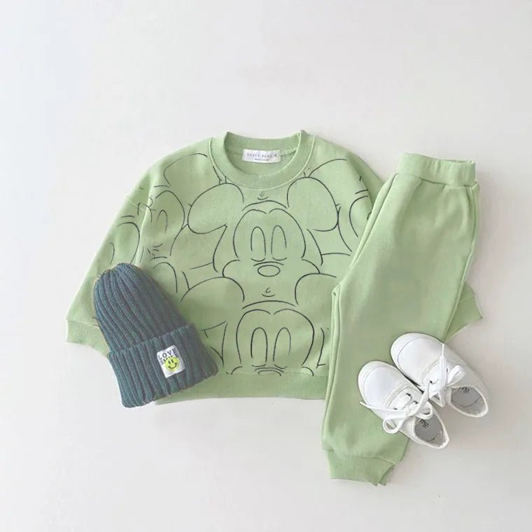 Green Mickey Mouse-themed sweatshirt, pants, blue beanie, and white sneakers.