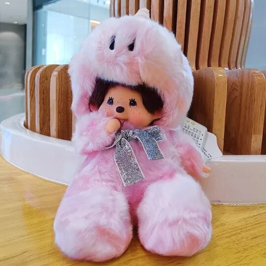 Pink plush toy with a hood and bow tie on a wooden chair.