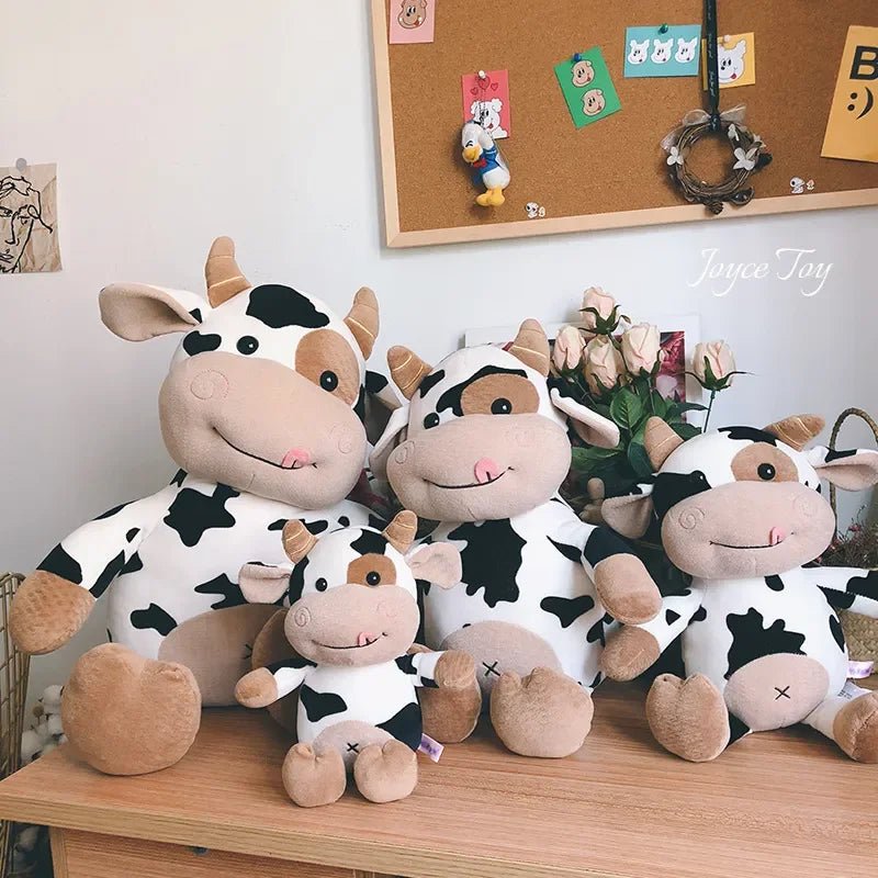 Four cow-themed plush toys on a wooden surface with a bulletin board in the background.