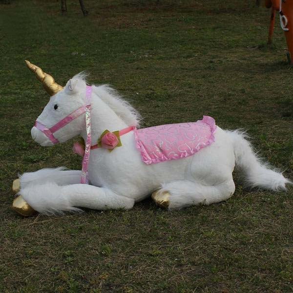 Plush unicorn toy with pink saddle and gold horn on grass