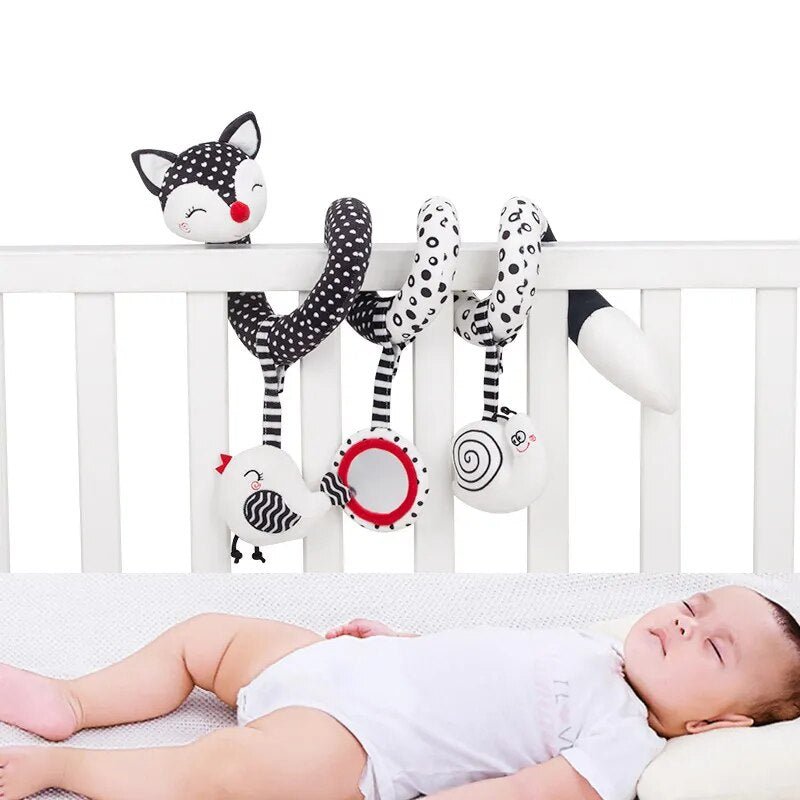 Baby lying in a crib with various animal-themed rattles hanging above.