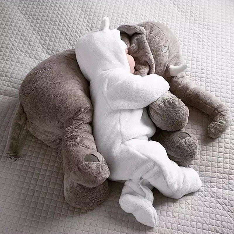 Plush elephant toy and baby in white outfit on a textured surface