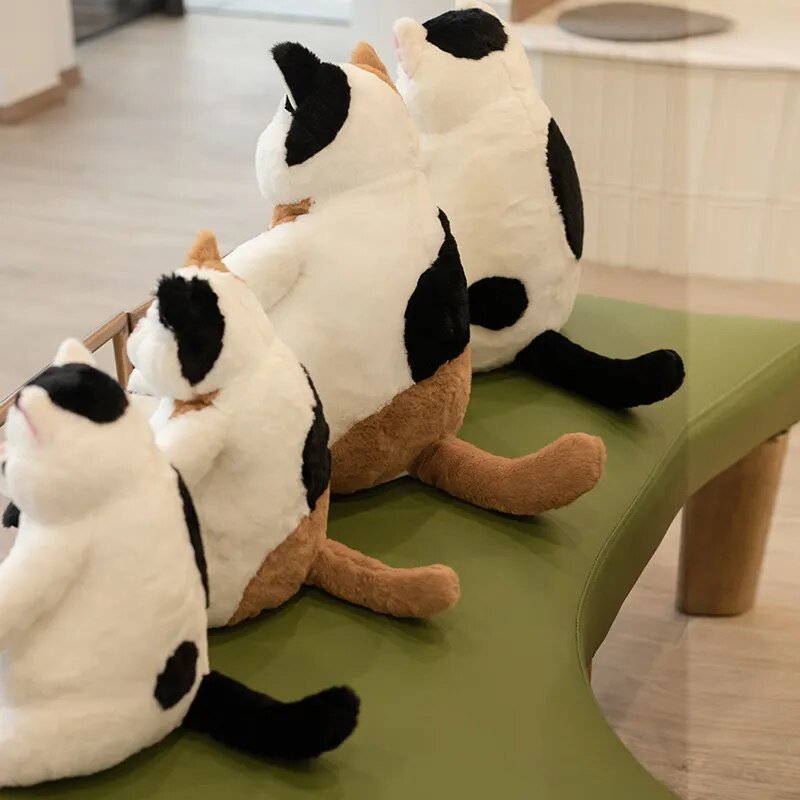 Plush toys resembling cats sitting on a green surface indoors.