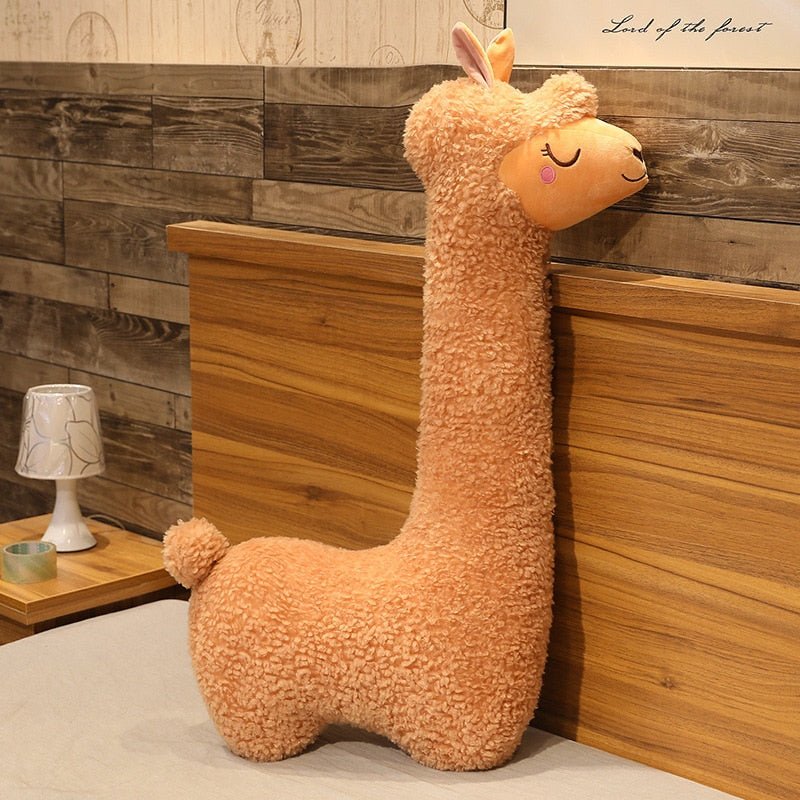 Plush llama toy against a wooden wall with a lamp and small table.