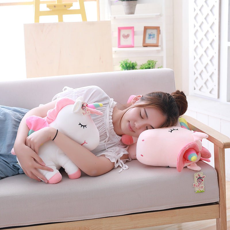Woman lying on a couch with plush toys, including a unicorn and a pink creature, in a bright room.